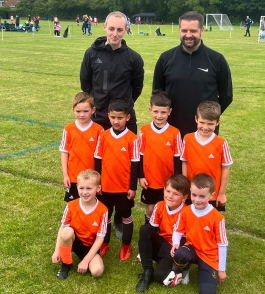A group of the Matthiola under 7s football team wearing an orange football kit with two of their coaches