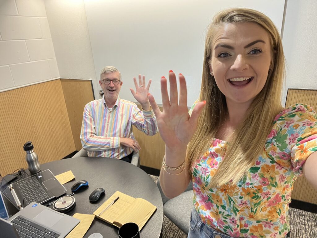 Our consultants Sophie and John at our Youth Conference virtual session. They are sat behind a desk with their laptops waving to camera.