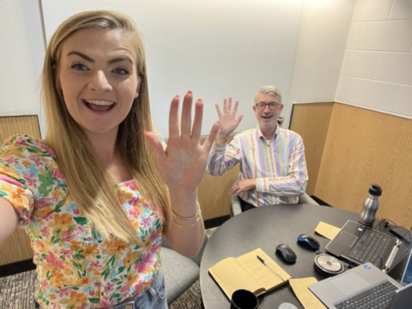 Our consultants Sophie and John at our Youth Conference virtual session. They are sat behind a desk with their laptops waving to camera.