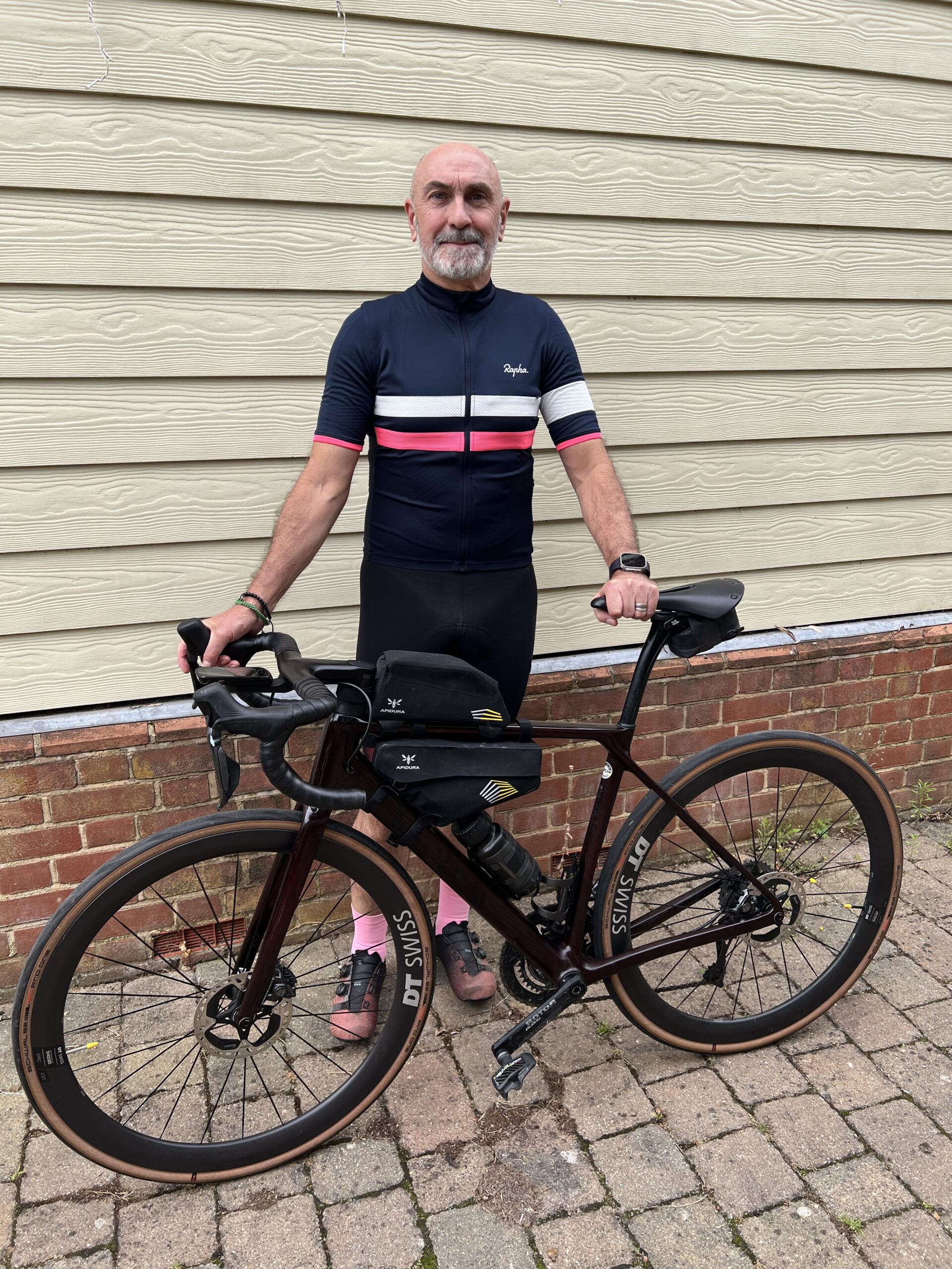 Our CEO, Tony Summers, standing in front of a wooden building in his cycling top.